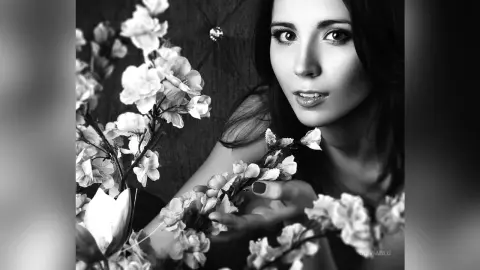Moody black and white portrait of a young woman surrounded by delicate white flowers.