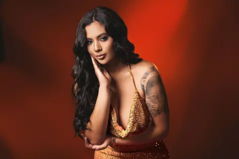 Elegant woman in a shimmering gold sequin dress posing against a warm red studio background.