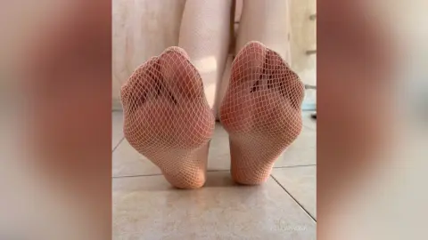 Close-up of feet wearing white fishnet stockings on a tiled floor in a bright indoor setting.