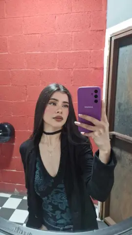 DashaRodriiguez poses in a mirror wearing a black blazer over a dark teal patterned tank top, with long dark hair and a black choker.