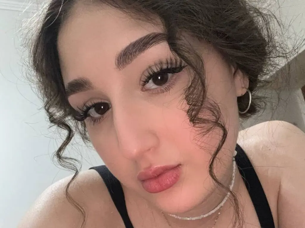 Close-up portrait of a young woman with curly hair and natural makeup wearing a black tank top in soft lighting.