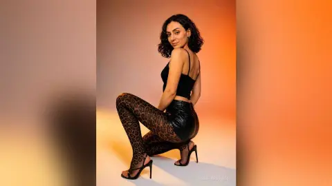 Stylish woman in a black crop top and leopard print leggings posing against a warm orange studio background.