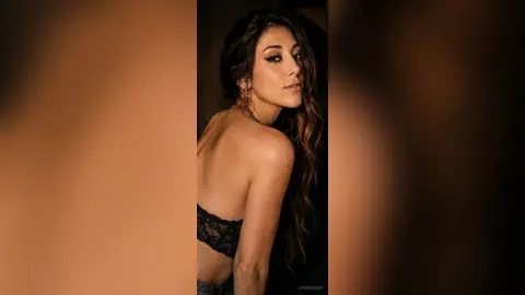 LorineSwan poses looking over her shoulder, showing her bare back and long brown hair while wearing black lace lingerie.