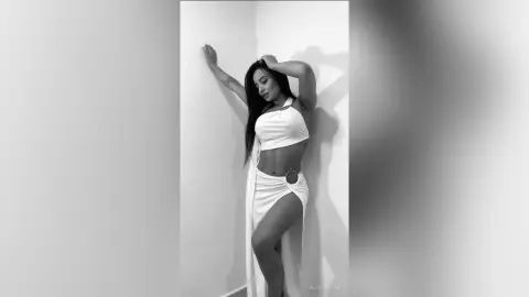 Elegant woman in a white halter cutout maxi dress posing against a minimalist wall in a moody black and white style.