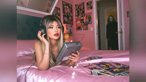 Blonde woman in black tank top listening to radio on pink bed in nostalgic retro bedroom with Ghostface in doorway.