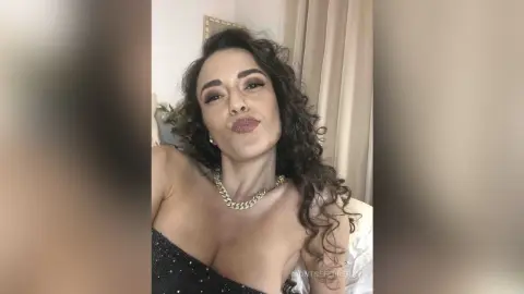 MontseFerrera pouts her lips while wearing a black sparkly tube top and a gold chain necklace.