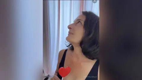 MichaelaBelle looks upward while wearing a black tank top against a white curtain background.