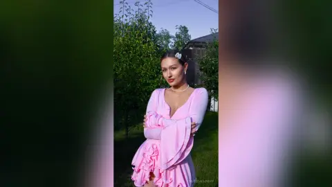 Young woman in a pink ruffled dress posing outdoors in a lush green garden during golden hour.