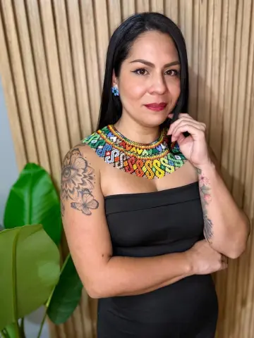 Smiling woman in a black strapless dress and colorful beaded statement necklace standing by a wooden wall.