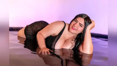 Smiling woman in a black sequin dress lounging by a reflective pool in soft pink lighting.