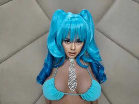 Woman with bright blue pigtails wearing a turquoise bikini and silver rhinestone tie in a soft studio setting.