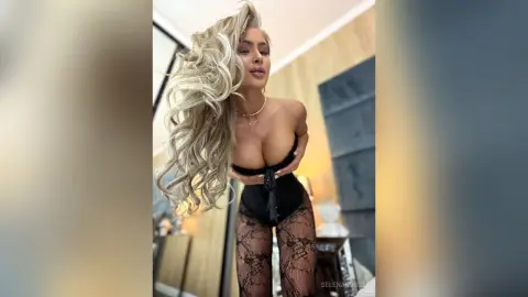 Blonde woman in black lace lingerie posing in a modern bedroom with a glamorous mood.