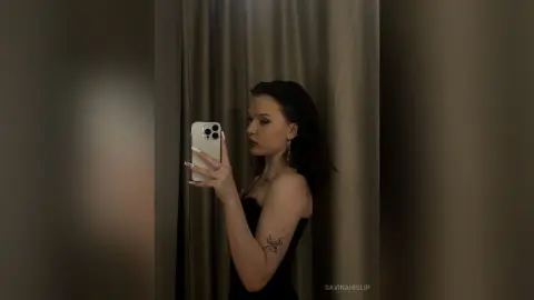 Young woman in a black strapless dress taking a moody mirror selfie in a dimly lit room.