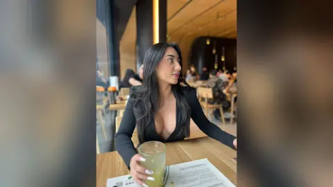 Elegant woman in a black long-sleeve dress sitting at a cafe table with a refreshing green drink.