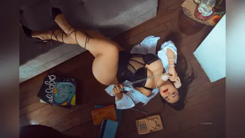 Glamorous woman in black lingerie lying on a wooden floor with a vintage telephone in a moody setting.