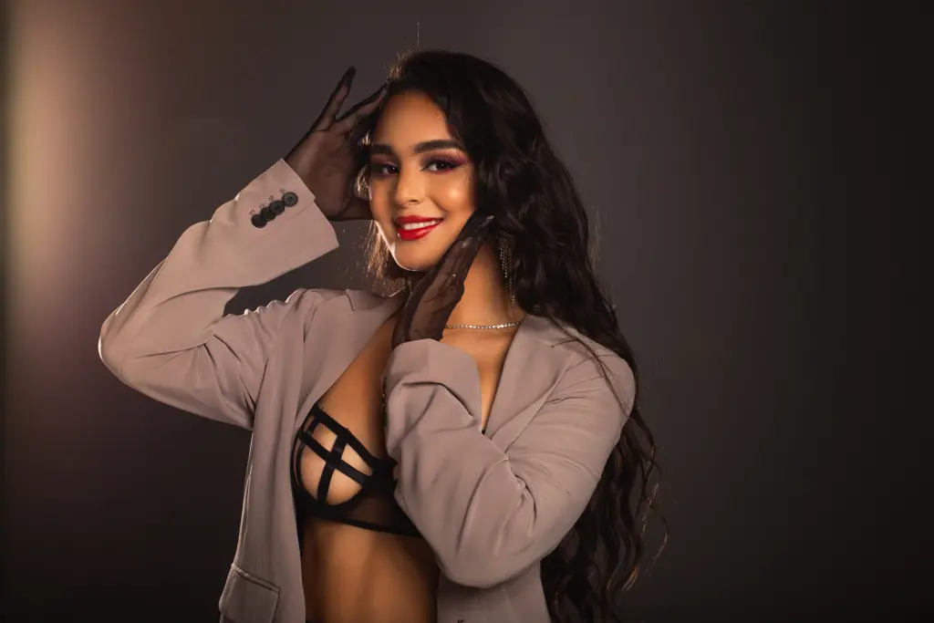VictoriaPeach19 poses in a white feathery outfit with her long dark hair, posing against a soft purple and white background.