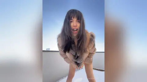 Cheerful woman in a brown faux fur coat laughing outdoors under a clear blue sky.