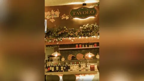 Warm interior of Tavolo restaurant featuring a bar stocked with wine bottles and rustic decor.