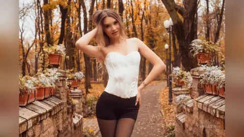 Blonde woman in a white corset and black shorts posing in an autumnal forest setting with a dreamy mood.
