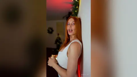 Cheerful redhead woman in a white sleeveless top holding a gift in a festive indoor setting.