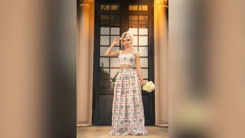 Elegant woman in a white floral print crop top and maxi skirt standing before a classic dark doorway.