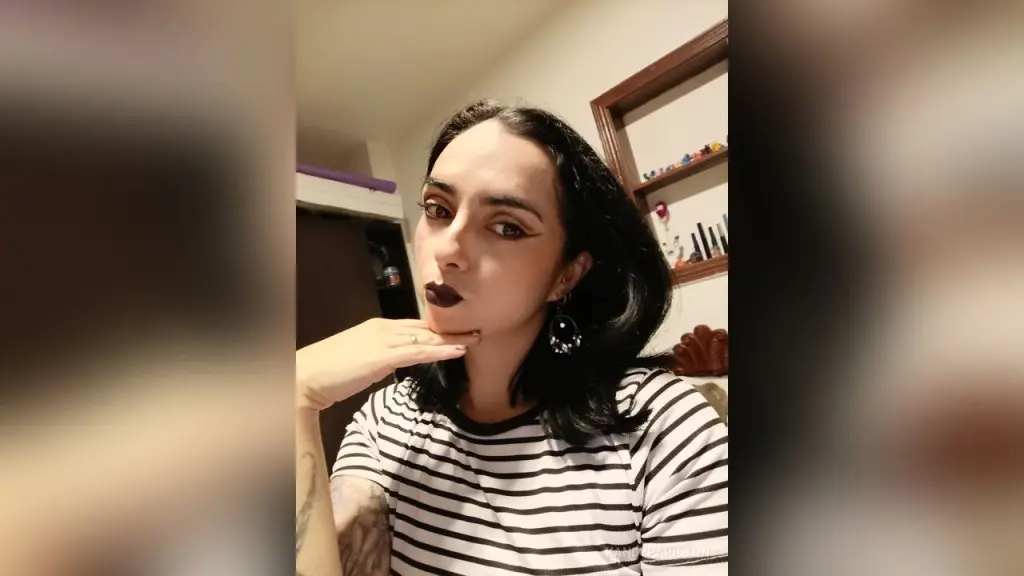 KandyPariston — Young woman with dark hair and bold lipstick wearing a striped shirt in a cozy indoor setting.