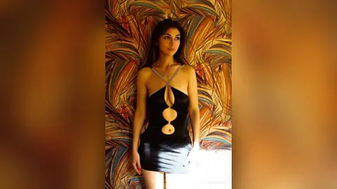 Elegant woman in a black cutout mini dress posing against a tropical leaf patterned backdrop.