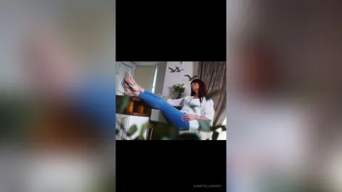 DonatellaRossy — DonatellaRossy sits on a white surface wearing a white shirt and blue jeans with her legs raised up.