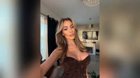 Glamorous woman in a brown corset top posing in a bright, modern living room.