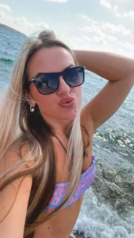 Blonde woman in sunglasses and pink patterned bikini relaxing on a boat in the sunny ocean.