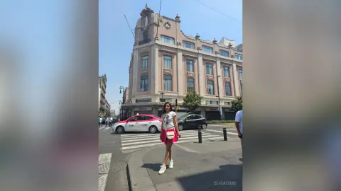 Young woman in a white t-shirt and pink skirt standing on a sunny city street by a classic European building.