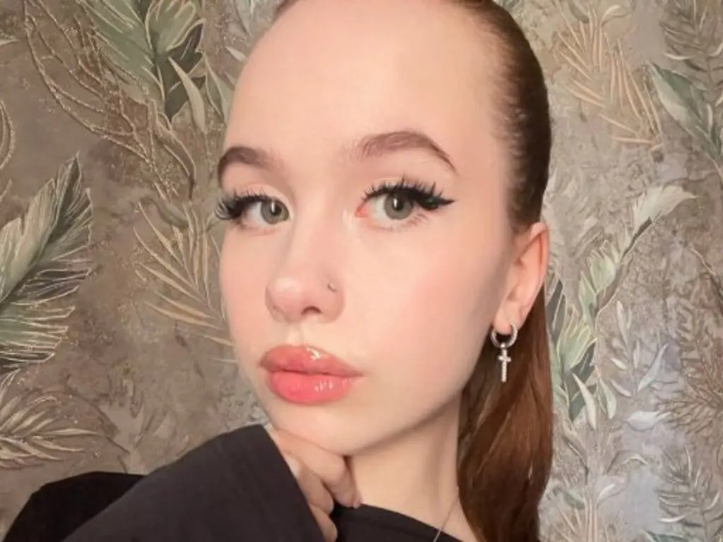 Close-up portrait of a young woman with winged eyeliner and silver hoop earrings against a leafy wallpaper background.