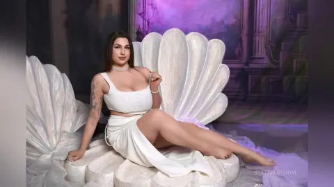 BettyBlossom — BettyBlossom sits in a large white seashell chair wearing a white crop top and matching skirt.