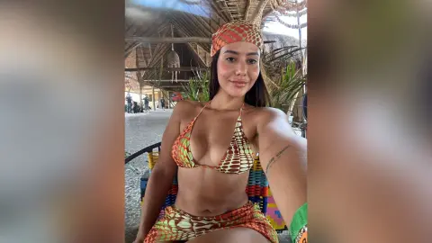 Smiling woman in a colorful patterned bikini and headscarf relaxing at a tropical beach resort.