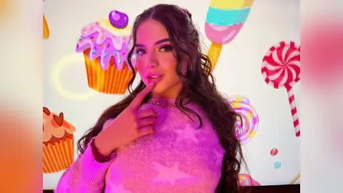 ValeryRouge poses with a finger to her lips, wearing a pink sweater against a white background with colorful cupcake and lollipop illustrations.