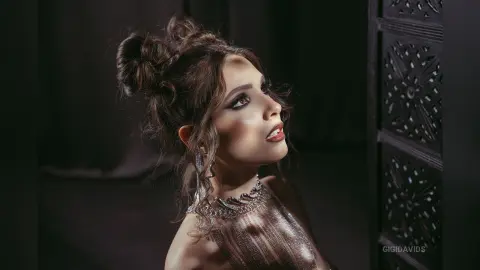 Elegant woman in a shimmering silver gown and statement jewelry posing with a moody, glamorous expression.