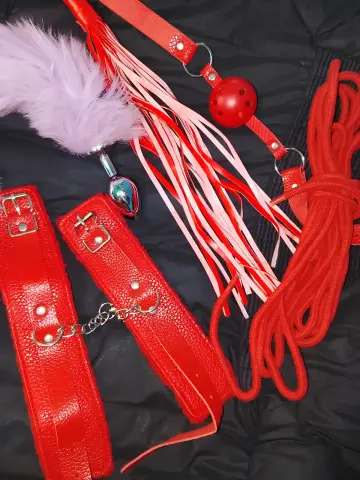 Red leather bondage gear set featuring a whip, harness, and textured straps on a black background.