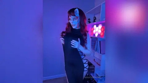 Woman in black cosplay outfit and fox mask posing in a room with neon purple lighting.