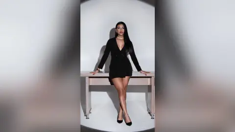 Elegant woman in a chic black blazer dress posing confidently against a minimalist white studio background.