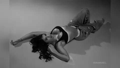 Moody black and white portrait of a woman in a black Calvin Klein bralette and denim jeans lying on a studio floor.