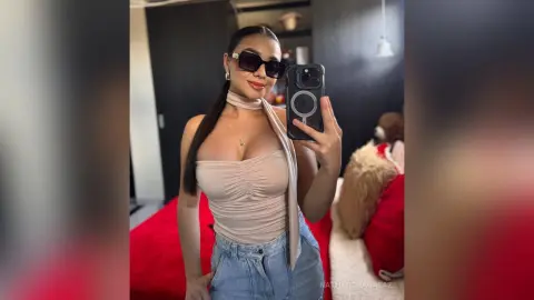 Stylish woman in a beige bodysuit and sunglasses posing confidently in a modern indoor setting.