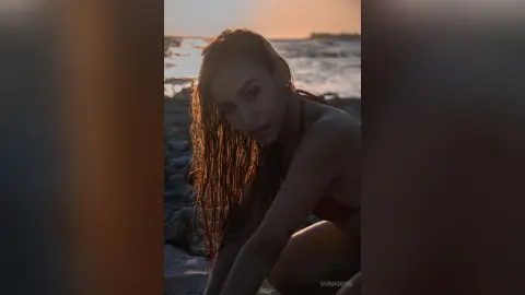 Beautiful woman in red swimwear posing on a rocky beach during a golden sunset mood.
