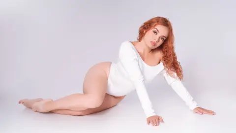 Curvy redhead woman in a white long-sleeve bodysuit posing gracefully on a white studio background.