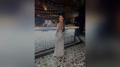 Elegant woman in a white lace evening gown standing in a stylish modern bar with patterned tile flooring.