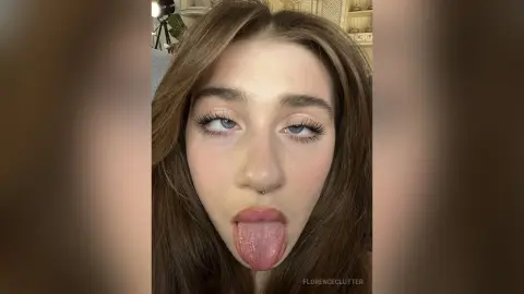 Young woman with long brown hair and winged eyeliner sticking her tongue out in a playful close-up portrait.