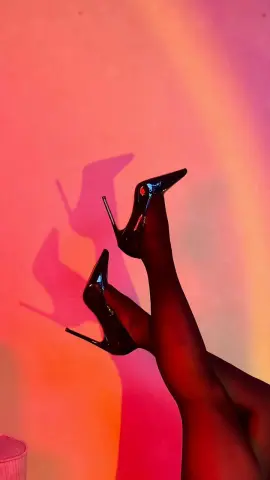 Woman in black tights and high heels posing against a warm red and orange studio background.