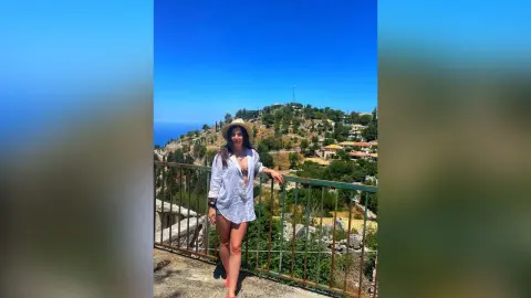 Young woman in a white linen shirt and sun hat enjoying a sunny summer day overlooking a Mediterranean hillside.