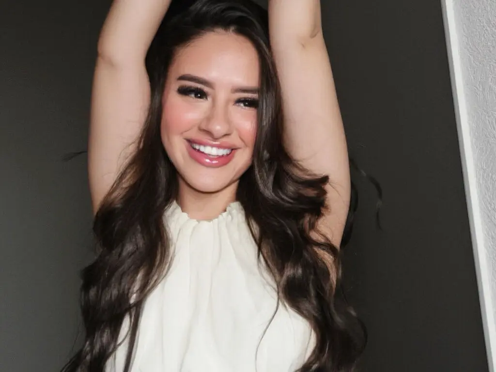 Smiling brunette woman in a white sleeveless top posing happily against a dark background.