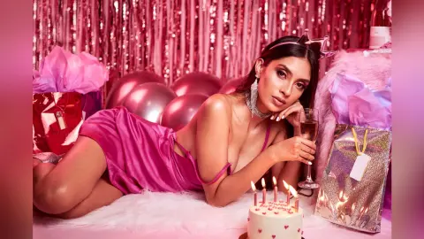 LucyMartin lies on white faux fur wearing a pink satin slip dress, holding a glass of champagne next to a lit birthday cake.