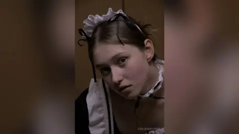 Young woman in a vintage black and white maid outfit with a ruffled headband looking thoughtfully at the camera.